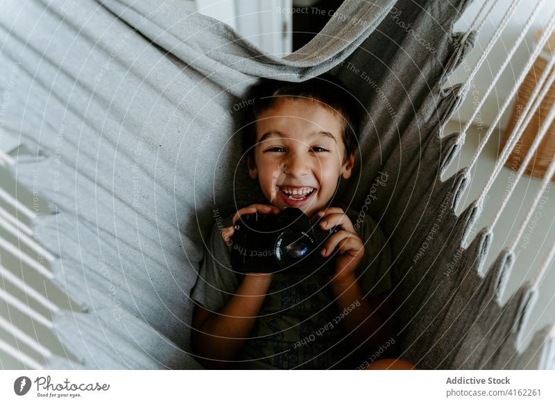 Excited boy with photo camera laying in home hammock laugh excited photographer hobby expressive rest joy contemporary device photography gadget equipment