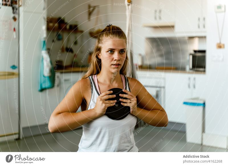 Focused young sportswoman doing exercise with weight at home training plate concentrate determine energy wellbeing vitality wellness female sportswear kitchen