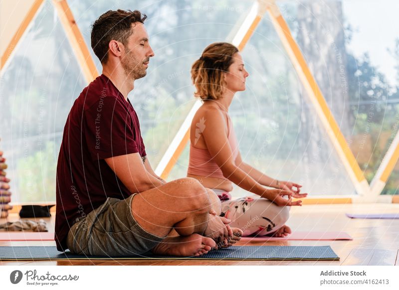 Couple sitting in Lotus pose while meditating on yoga mat couple lotus pose meditate legs crossed eyes closed zen spirit energy mindfulness class barefoot fit