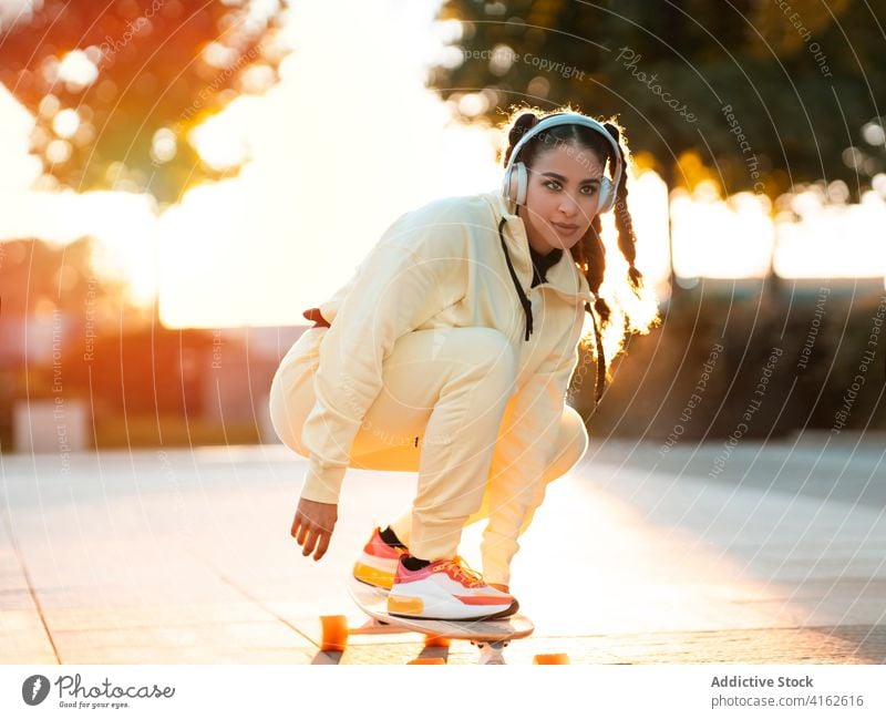 Trendy female millennial listening to music while riding longboard in park woman ride positive active trendy joy modern sunset young ethnic sportswear