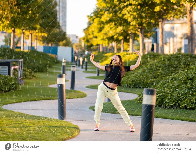 Flexible young woman dancing in park dance pathway active ballerina trendy flexible city move energy cool hobby female style outfit hairstyle sneakers modern