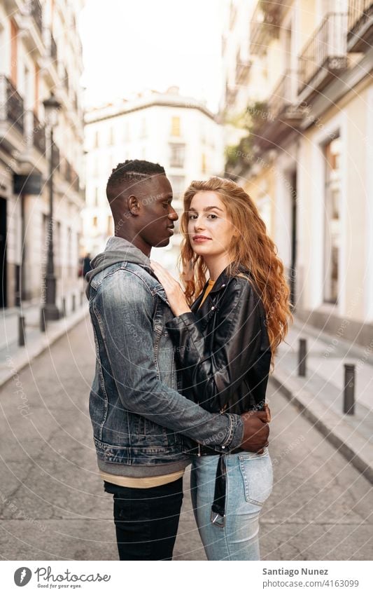 Loving Multiethnic Young Couple looking at camera standing street hugging front view portrait relationship multi-racial black man caucasian multi-cultural