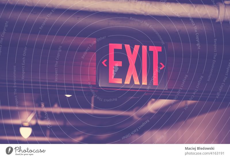 Illuminated exit sign, selective focus, color toning applied. illuminated light symbol red safety fire escape security industrial indoors emergency direction