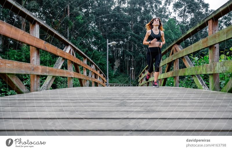 Woman running through an urban park sportswoman tired effort wooden walkway endurance persevere constancy determined athlete cheerful runner fitness female