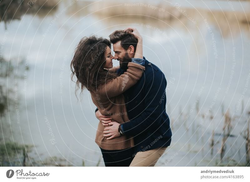 two caucasian lovers near the lake. Young couple is hugging on autumn day outdoors. A bearded man and curly woman in love. Valentine's Day. Concept of love