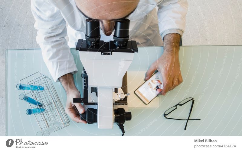 Mature scientist male wearing a lab coat looking through a microscope in a laboratory. Science concept. Laboratory scientific Scientist expertise innovation