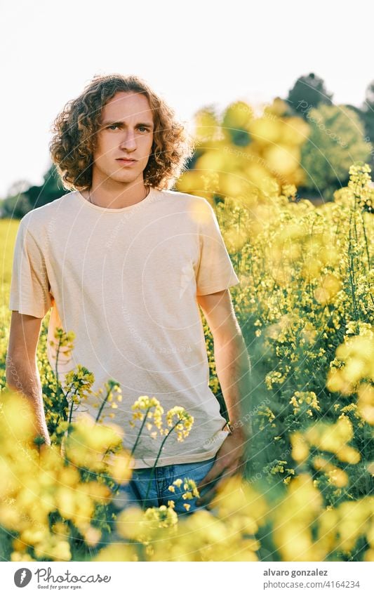 a young man surrounded with yellow flowers in a sunny spring day rapeseed nature landscape che male portrait guy handsome person attractive caucasian casual one