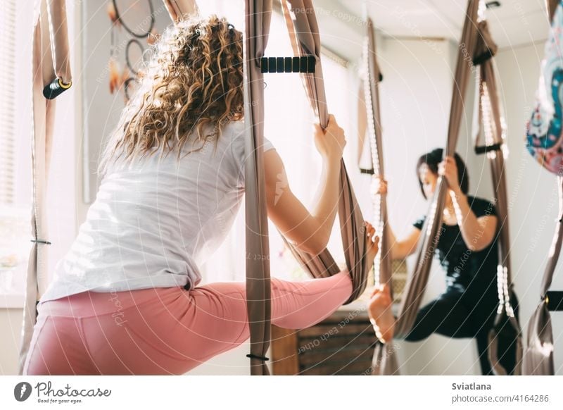 A girl with curly hair practices yoga with a hammock. Yoga, aero yoga, fitness, lifestyle. Rear view aerial woman young antigravity asana balance health