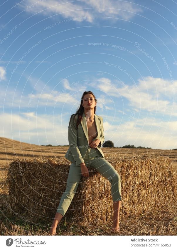 Fashionable young woman resting on haystack in countryside confident style fashion sensual naked nature model tranquil female slim suit barefoot body bale
