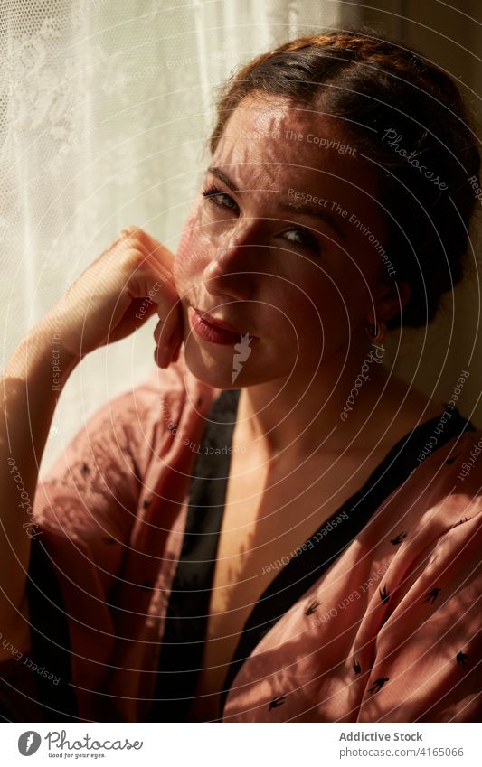 Pensive young woman relaxing near window at home rest dreamy pensive hand on cheek style feminine appearance sunlight female outfit tranquil trendy calm elegant