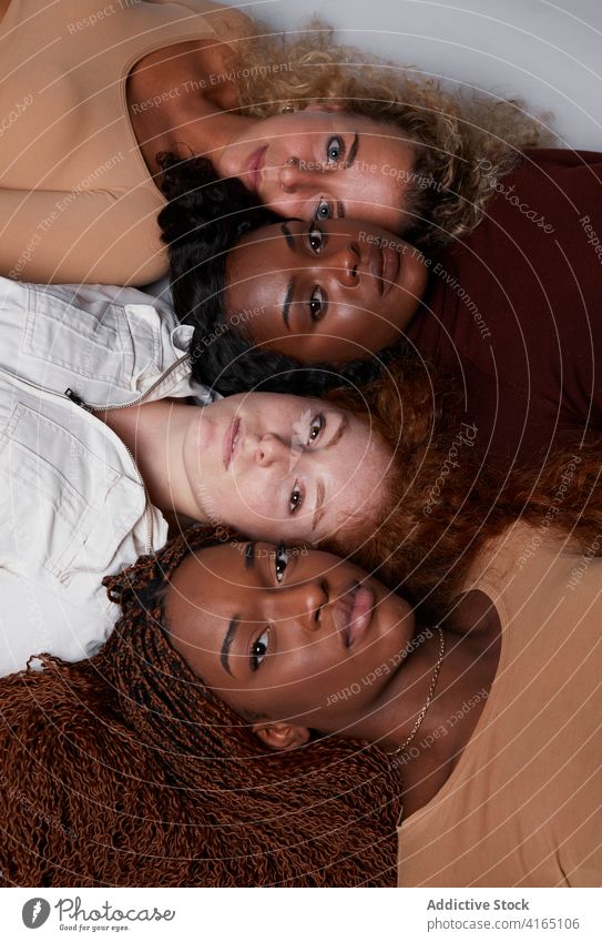Multiracial women lying in row in studio together model pastel color outfit curly hair multiethnic multiracial diverse black african american line floor rest