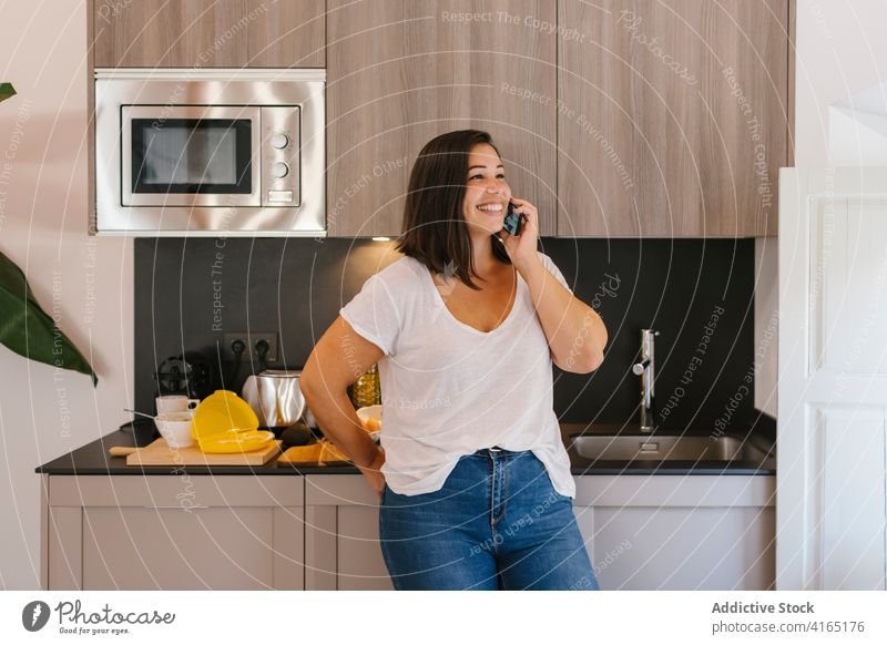 Smiley woman talking on the phone in a kitchen indoors home house girl avocado shopping bag dining room coffee breakfast morning caucasian brunette table