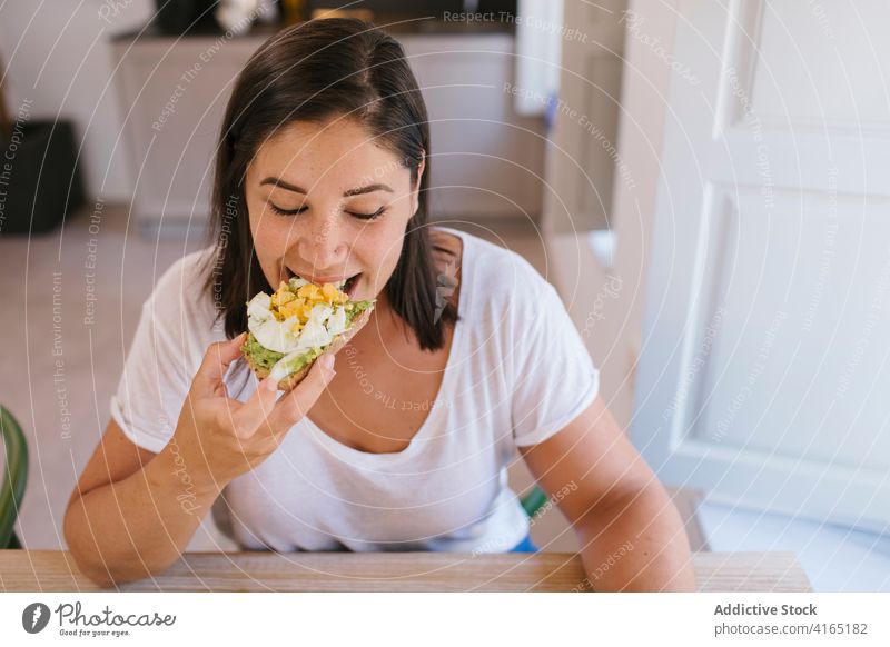 Woman biting a breakfast toast indoors home house girl woman avocado shopping kitchen coffee morning caucasian brunette table lifestyle casual eating food