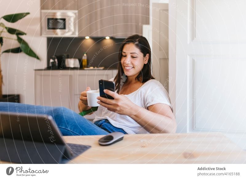 Smiley girl using a smartphone in the kitchen indoors home house woman shopping coffee breakfast morning caucasian brunette table lifestyle casual food