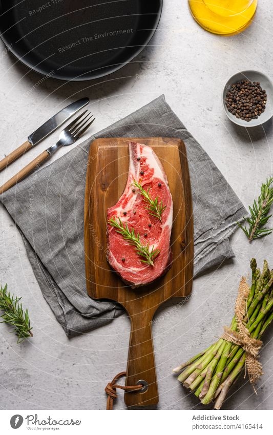 Raw beef steak with herbs on cutting board raw bone t bone rosemary garnish meat pepper black wooden kitchen cook food cuisine delicious dish spice gourmet
