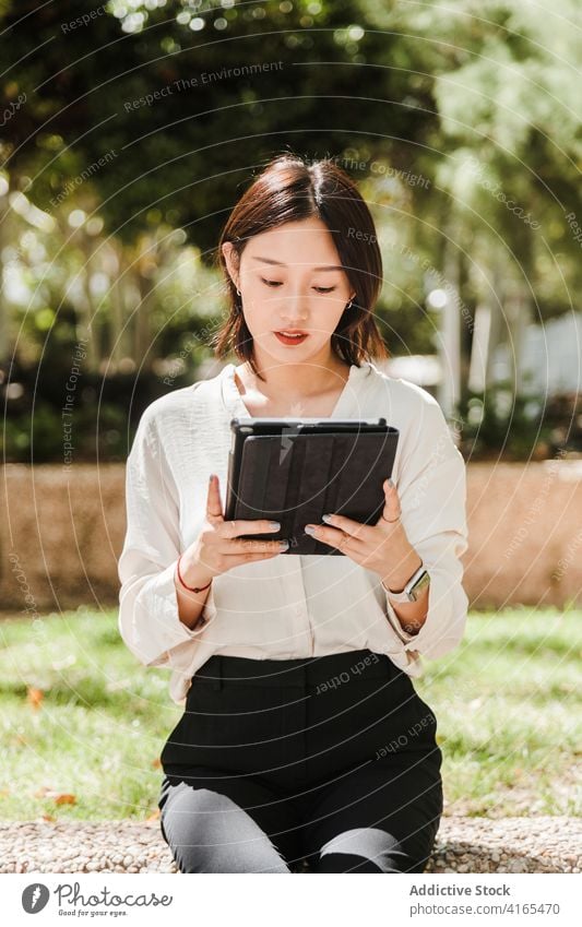 Young ethnic woman working remotely on tablet in park attentive new normal coronavirus job busy gadget using browsing female young asian formal mask covid 19