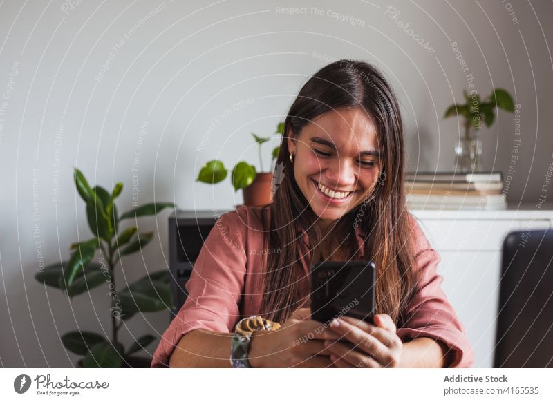 Excited young woman browsing modern smartphone at home excited toothy smile delight surfing mobile device internet casual message sms happy using communicate