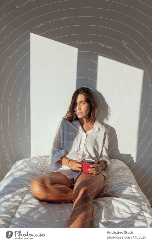 Cheerful young woman drinking coffee in bed morning smile happy sensual comfort allure cozy joy female white shirt body barefoot home beverage sunny relax rest