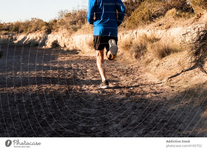 Anonymous sportsman jogging on sandy terrain in mountainous terrain run semi desert hill training active jogger healthy nature wellbeing exercise workout male