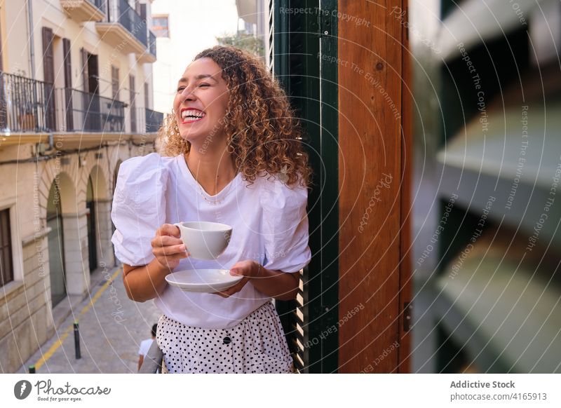 Happy woman enjoying hot drink on balcony rest laugh style hotel weekend break happy female relax cheerful delight cup beverage curly hair smile tea coffee