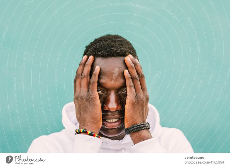 Portrait of young african black man against a green wall with white sweatshirt with his hands on his face. Stop racism protest concept. BLM afro street stop blm