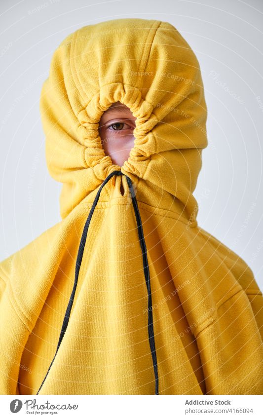 Unrecognizable teen hiding in hood in studio cover hide having fun yellow hoodie teenage style expressive playful childish carefree funny individuality cool