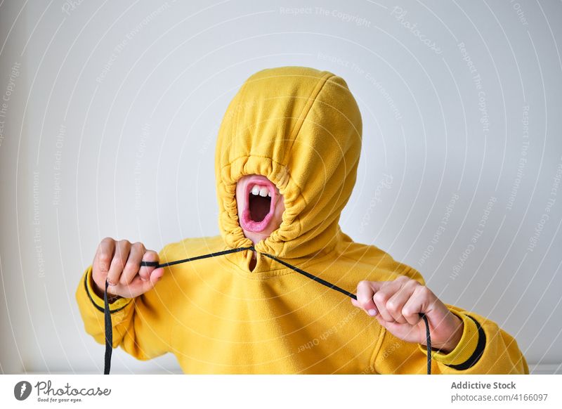 Expressive teen in yellow hoodie in studio teenage rebel scream make face color mouth opened bright vibrant cover face crazy energy grimace shout style shock