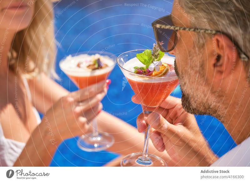Unrecognizable couple resting near swimming pool with cocktails clink drink poolside enjoy happy love relationship relax vacation holiday summer boyfriend