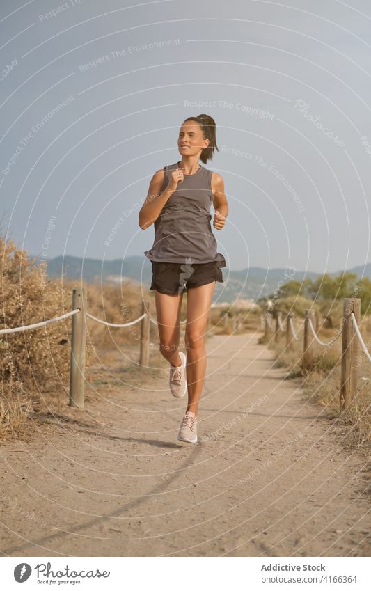 Strong woman running on countryside sandy coast strong activewear athletic fast jog shore female empty shrub dry young exercise fitness healthy sporty lady