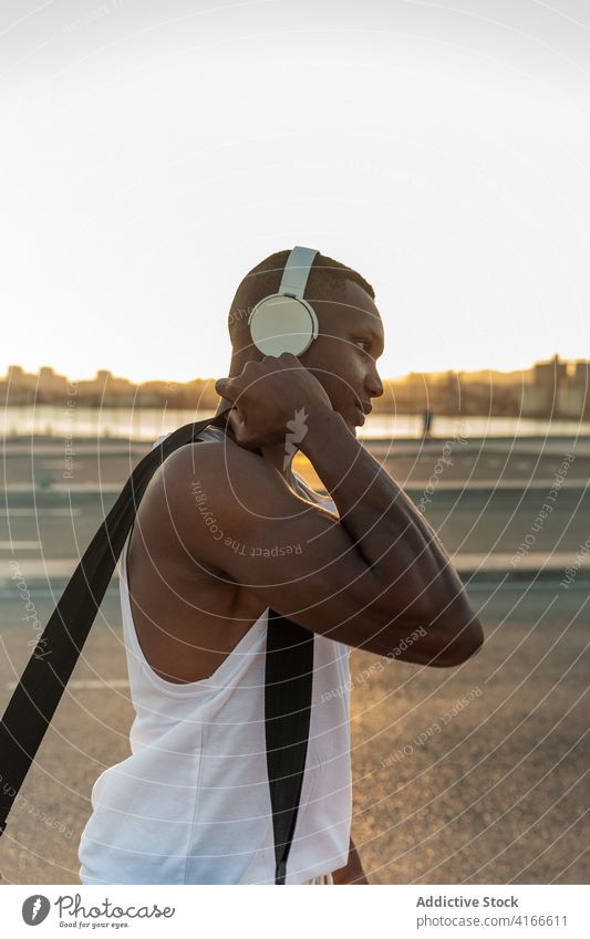 Black sportsman in headphones resting after training athlete serious muscular sporty music listen fit male sportswear lifestyle wellbeing device activity
