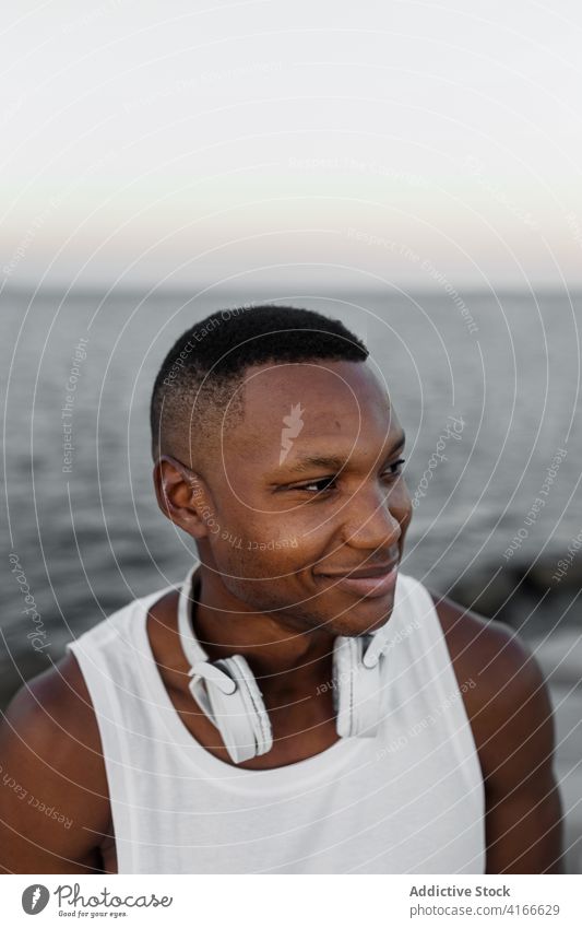 Cheerful ethnic man smiling standing on coast of sea excited headphones positive carefree shore enjoy happy cheerful male beach rest water freedom pleasure