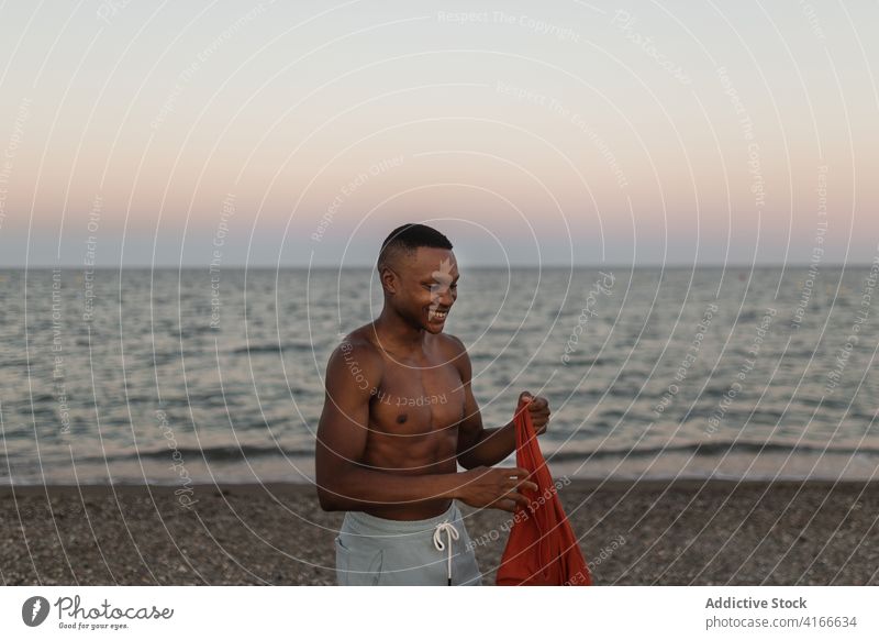 Smiling black man putting on t shirt on beach smile happy put on rest glad athlete coast carefree seashore male runner lifestyle relax water positive