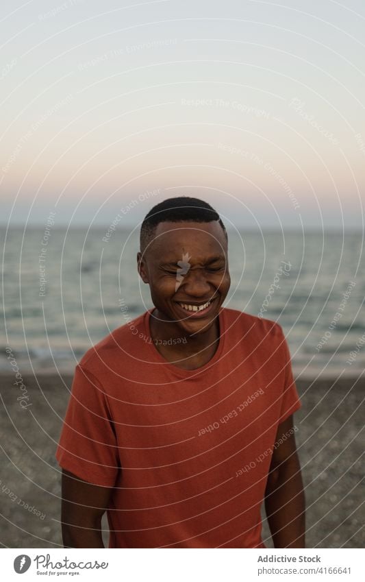 Cheerful black sportsman standing on beach african smiling closed eyes fit strong male sporty serious guy muscle shore confident torso african american seashore