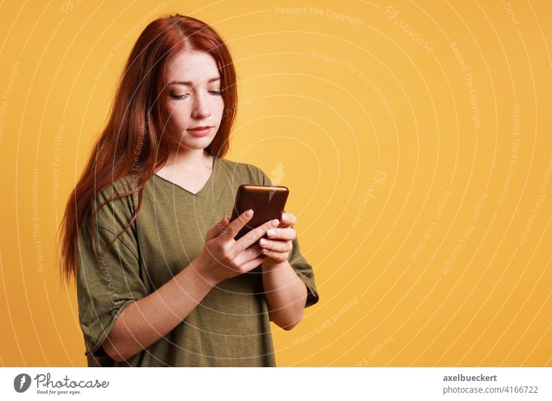 young woman reading text message on smartphone or mobile cell phone person girl adult using serious people female caucasian long red hair casual lady copyspace