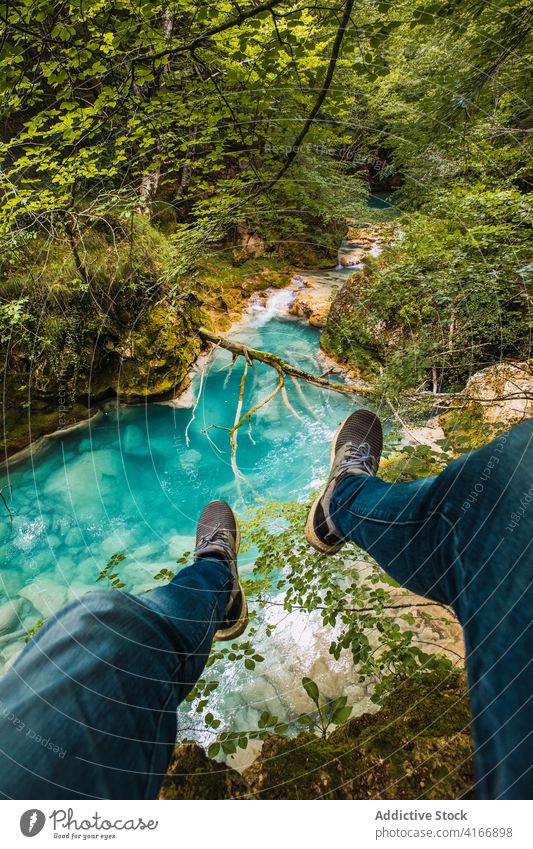 Faceless traveler enjoying river and pond from mountain tourist admire nature highland flow vegetate bright contemplate sneakers jeans tree environment ripple
