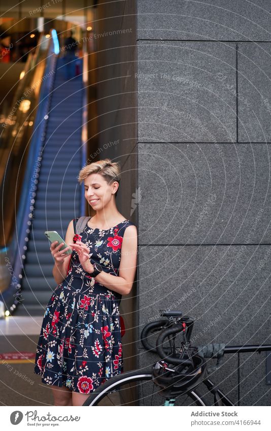 Young woman with phone in hands stands near modern building, escalator Woman dress bike evening walk girl young riding beautiful city blurred bokeh defocused