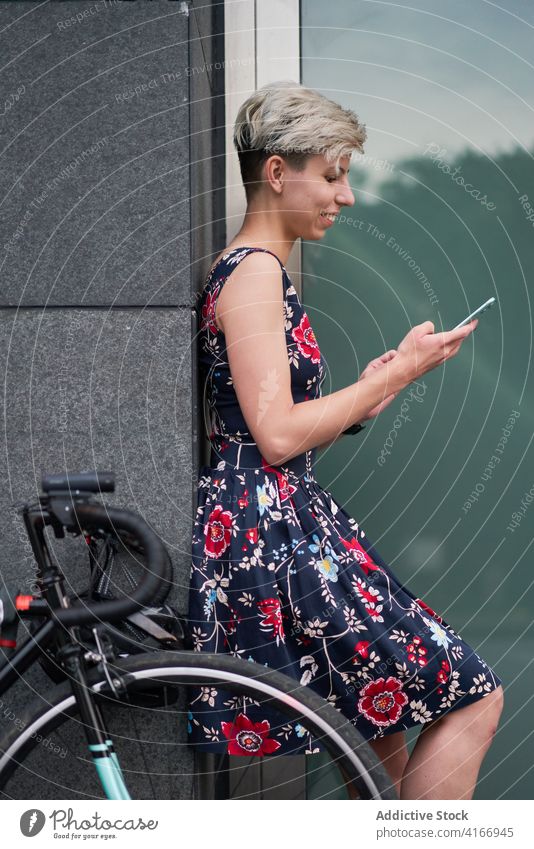 Side view of woman with phone in hands stands near modern building Woman dress bike evening walk girl young riding beautiful city smartphone holds