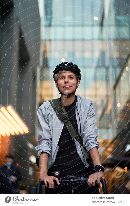Woman in helmet on bicycle near tall building with glass windows Cyclist bricked city day woman young sports riding summer protective girl delivery courier