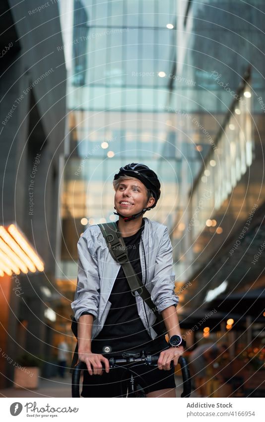 Closeup of woman in helmet on bicycle looking to side near tall building Cyclist bricked city day young sports riding summer protective girl delivery courier