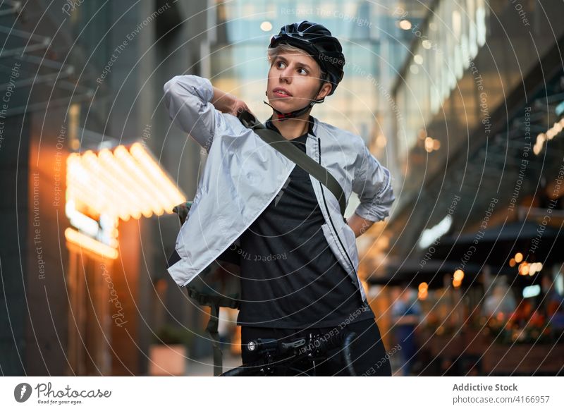 Closeup of girl in helmet on bicycle looking to side near tall building Cyclist bricked city day woman young sports riding summer protective delivery courier