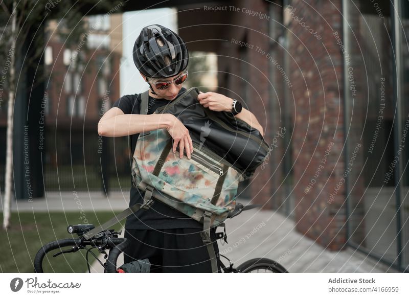Female courier with bag in his hands on street Cyclist building bricked city day woman young sports riding summer helmet protective sunglasses girl delivery