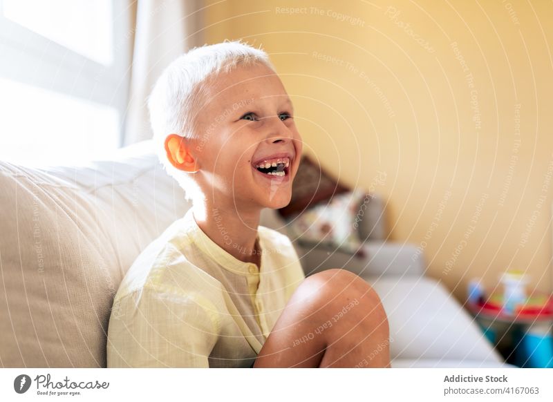 Positive child smiling while resting on sofa at home relax couch smile cheerful free time positive adorable childhood joy comfort kid blue eyes blond delight