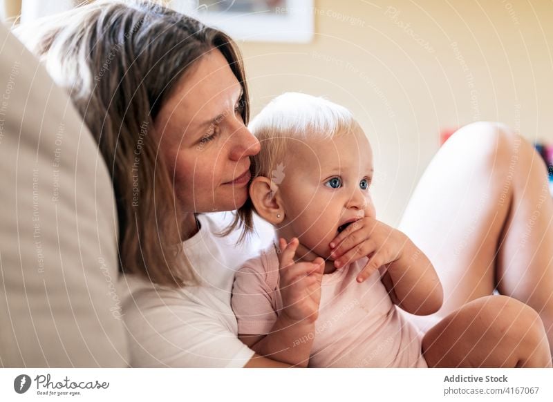 Calm mother embracing infant daughter on sofa woman hug baby couch home happy love embrace eyes closed bonding care adult motherhood cute adorable parent