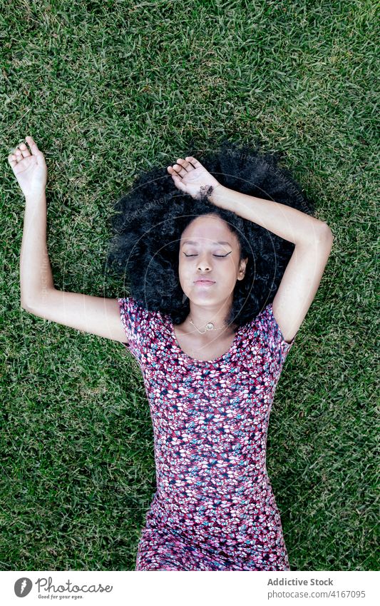 Tired woman lying on grass in park sleep relax carefree dreamy summer enjoy female ethnic black african american afro hairstyle dress lush lawn green