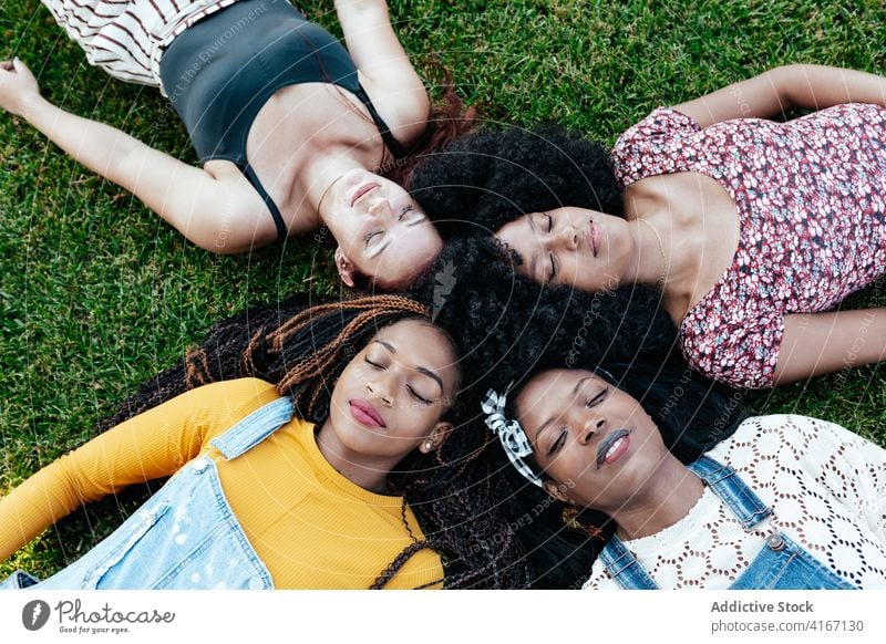 Diverse women lying on grass in park friendship positive together friendly bonding young multiethnic multiracial diverse black african american green lawn