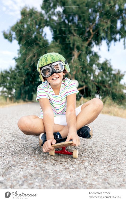 Happy boy on skateboard in protective eyeglasses helmet goggles having fun carefree childhood excited content road stylish apparel decorative summer trendy