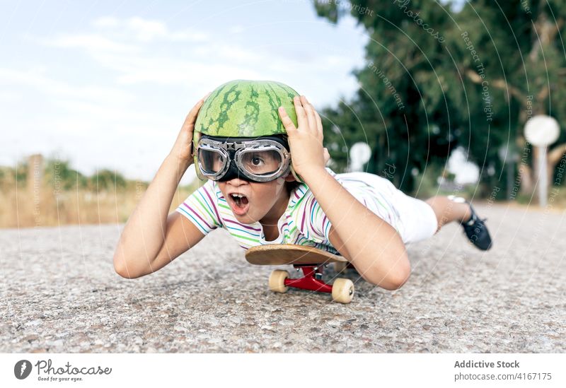 Positive kid on skateboard in safety glasses and decorative helmet boy having fun carefree enjoy mouth opened activity road goggles childhood excited content