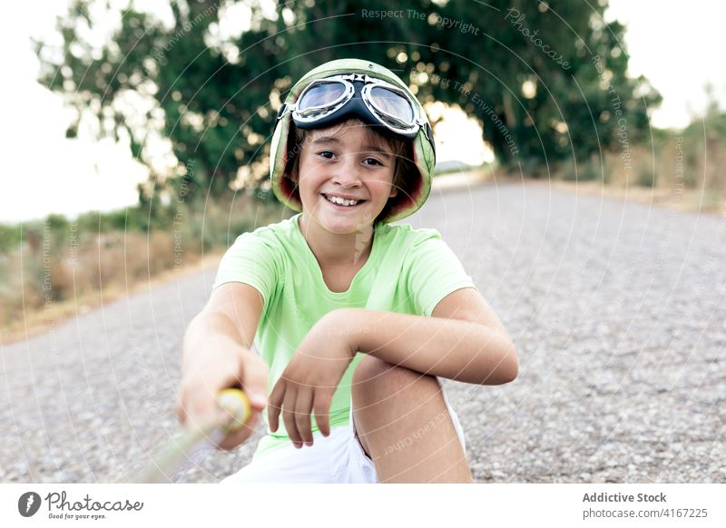 Glad boy on skateboard taking selfie on smartphone helmet glasses glad childhood free time road using gadget device cellphone sit rest watermelon cheerful kid