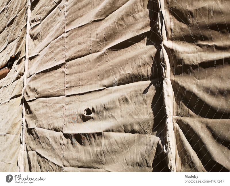 Folded tarpaulin in natural colours in the sunshine in front of scaffolding during the renovation of a historical building in the old town of Bielefeld in the Teutoburg Forest in East Westphalia-Lippe