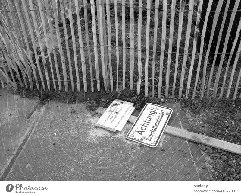 Fallen sign at a construction site entrance in front of a wooden fence at the harbour garden in Offenbach am Main in Hesse, photographed in classic black and white